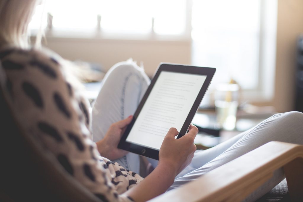 Femme assise dans un fauteuil qui lit un livre sur une tablette